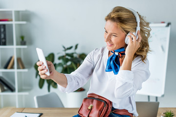 Wall Mural - beautiful businesswoman in headphones taking selfie with smartphone in office