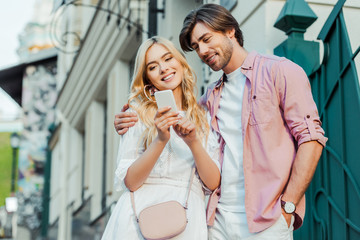 portrait of smiling young couple using smartphone together on street