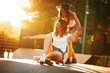 © BalanceFormCreative - Two female friends playing with skateboard at the skate park.One girl pushing other from behind.Laughing and fun.