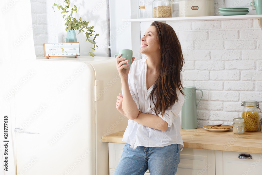 Young happy woman drinking coffee on the kitchen in the morning - obrazy, fototapety, plakaty 