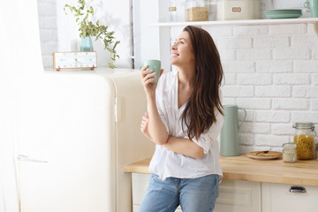 Young happy woman drinking coffee on the kitchen in the morning