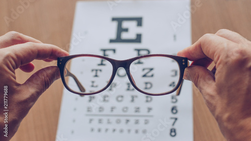 Cuadros en Lienzo Hands holding sight glasses in front of optician sight chart