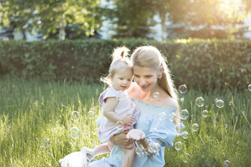 Happy family concept with young mother playing with her baby girl and making soap bubbles in the green park in nature, they smile and laugh, feel happy