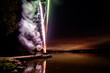 Fireworks on a dock over the water with smoke and lake horizon