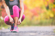© Maridav - Runner tying running shoes laces in autumn background. Athlete woman getting ready to run race in fall landscape with yellow leaves foliage in park.