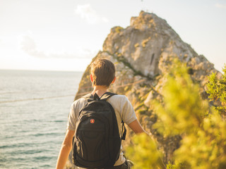 back view of man with backpack standint on the mountain in front of sea