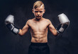 Young shirtless boy boxer with boxing gloves posing in a studio. Isolated on dark textured background.