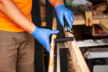 Close-up of a man with work clothes and protective gloves paints a wooden board