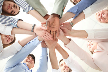 Wall Mural - People putting hands together on light background, bottom view. Unity concept