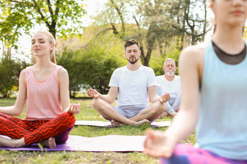 Group of people practicing yoga in park on sunny day