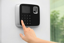 Young Woman Entering Code On Alarm System Keypad Indoors