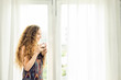 © pic for you - Young woman stand up near the window and looking up while drinking hot coffee.Happy woman relaxing at home in the morning.