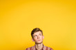 uncomprehending bewildered puzzled perplexed wondering man looking upwards. portrait of a young guy on yellow background pop up or peek out from the bottom. free space for advertising.