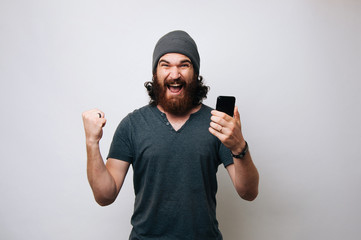 cheerful young bearded man wearing grey t-shirt and fur cap hat is surprised and happy. winner man w