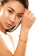 Close up studio portrait of a young Asian lady with nude make-up. The girl with a dainty golden bracelet on her wrist, one hand at her forehead, posing on the white background, looking at the camera.