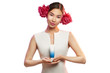 Close up portrait of a young Asian lady with two peony flowers in her hair. The beautiful girl standing on the white background, holding a tube with cosmetic product. Blank label for branding mock-up.