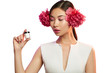 Close up portrait of a young Asian lady with peony flowers in her hair. The girl standing on the white background, holding a jar with cosmetic product, looking at it. Blank label for branding mock-up.