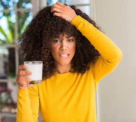 Wall Mural - African american woman holding a glass of milk stressed with hand on head, shocked with shame and surprise face, angry and frustrated. Fear and upset for mistake.