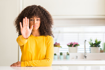 Sticker - African american woman wearing yellow sweater at kitchen doing stop sing with palm of the hand. Warning expression with negative and serious gesture on the face.