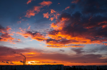 Colorful Magic Sunset. Roofs of city houses during sunrise. Birds flying in the sky. Dark smoke coming from the thermal power plant pipe.