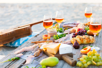 Picnic on beach at sunset in boho style. Romantic dinner, friends party, summertime, food and drink concept