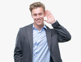 Young handsome blond business man smiling with hand over ear listening an hearing to rumor or gossip. Deafness concept.