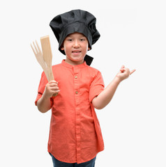 Dark haired little child wearing chef uniform very happy pointing with hand and finger to the side