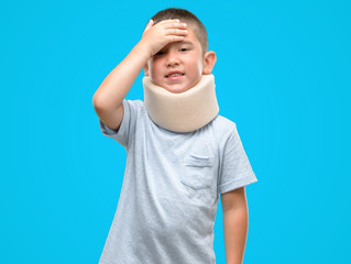 Wall Mural - Dark haired little child injured wearing neck collar stressed with hand on head, shocked with shame and surprise face, angry and frustrated. Fear and upset for mistake.