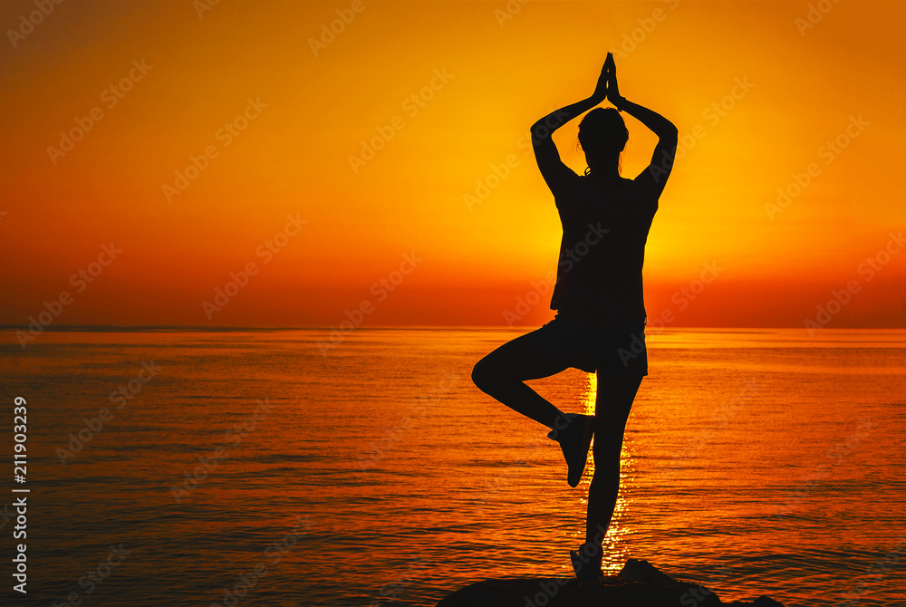 Silhouette of a girl in a yoga pose at sunset - obrazy, fototapety, plakaty 