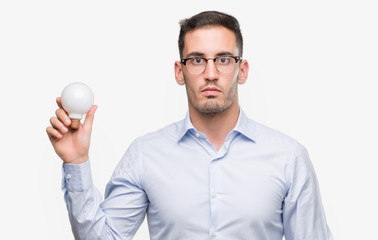 Poster - Handsome young man holding lightbulb as idea with a confident expression on smart face thinking serious