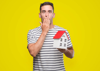 Sticker - Handsome real estate agent holding a house cover mouth with hand shocked with shame for mistake, expression of fear, scared in silence, secret concept