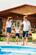 beautiful young family playing at poolside of cozy wooden cottage