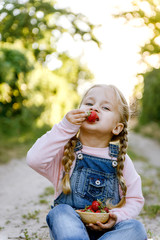 Wall Mural - little girl is sitting on the grass and eating strawberries