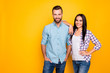 Portrait with copyspace of trendy cool couple in pants casual shirts looking at camera isolated on vivid yellow background. Advertisement concept
