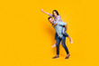© deagreez - Full size portrait of playful carefree couple in piggy back style making super man sign with raised fist isolated on bright yellow background