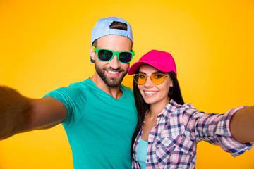 Poster - Self portrait of stylish trendy students in modern eyeglasses colorful headwear shooting selfie on front camera having beaming smiles isolated on bright yellow background