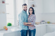 © deagreez - Portrait of attractive beautiful couple with modern hairstyle in casual clothes hugging looking at camera standing in modern white kitchen with interior