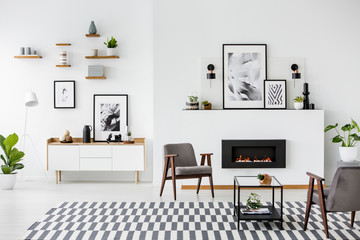 patterned carpet and grey armchairs in white living room interior with gallery of posters. real phot
