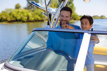 Wall Mural - Precious bonding. Happy young man hugging his beloved little son while they sailing the motorboat together