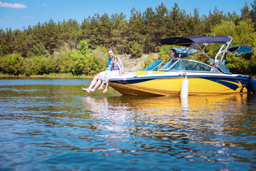 Sticker - Perfect family day. Pleasant young family enjoying the sunny day on the motorboat while father and his little daughter sitting on the bow of the boat together