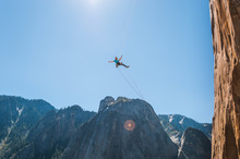 Person Swinging Mid Air Against Blue Sky On Alcove Swing At The Base Of El Capitan, Yosemite Valley, California, USA