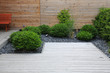 canvas print picture - Moderner Gartenbau und Terrassengestaltung: Terrasse aus Holz und Pflanzen im pflegeleichten Schotterbett vor einer Holzwand 