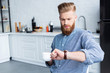 © LIGHTFIELD STUDIOS - handsome bearded young man holding cup of coffee and checking wristwatch
