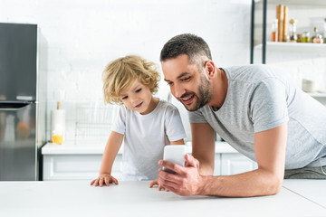 happy man showing smartphone screen to adorable son at kitchen