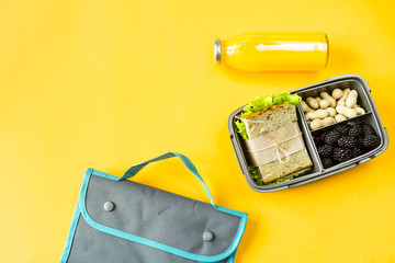 Lunchbox with food - a sandwich, nuts and berries - next to a bottle of orange juice and a bag for a luncheon. Food you can take with you. Top view, flat lay,