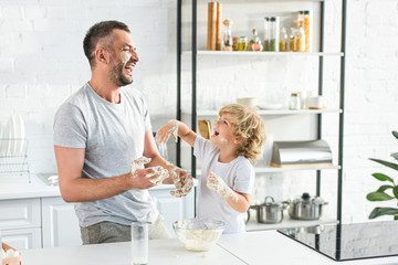 Wall Mural - smiling father and son get covering by dough and having fun at kitchen