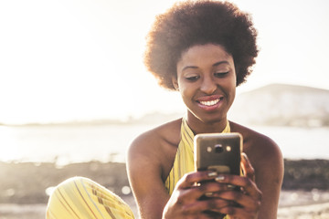 beautiful young model girl black rac african hair use mobile phone technology to write friends during a vacation. ocean and backlight in background, outdoor leisure activity modern