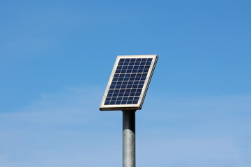 small solar panel mounted high on top of thick grey metal pole on warm sunny winter day with clear b
