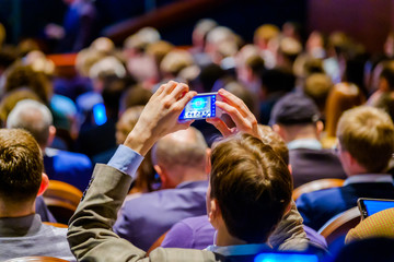 Man takes a picture of the presentation at the conference hall using smartphone