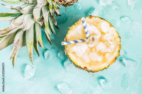 Summer refreshment drink concept, tropical pineapple cocktail or juice in pineapple with ice, light blue concrete background copy space